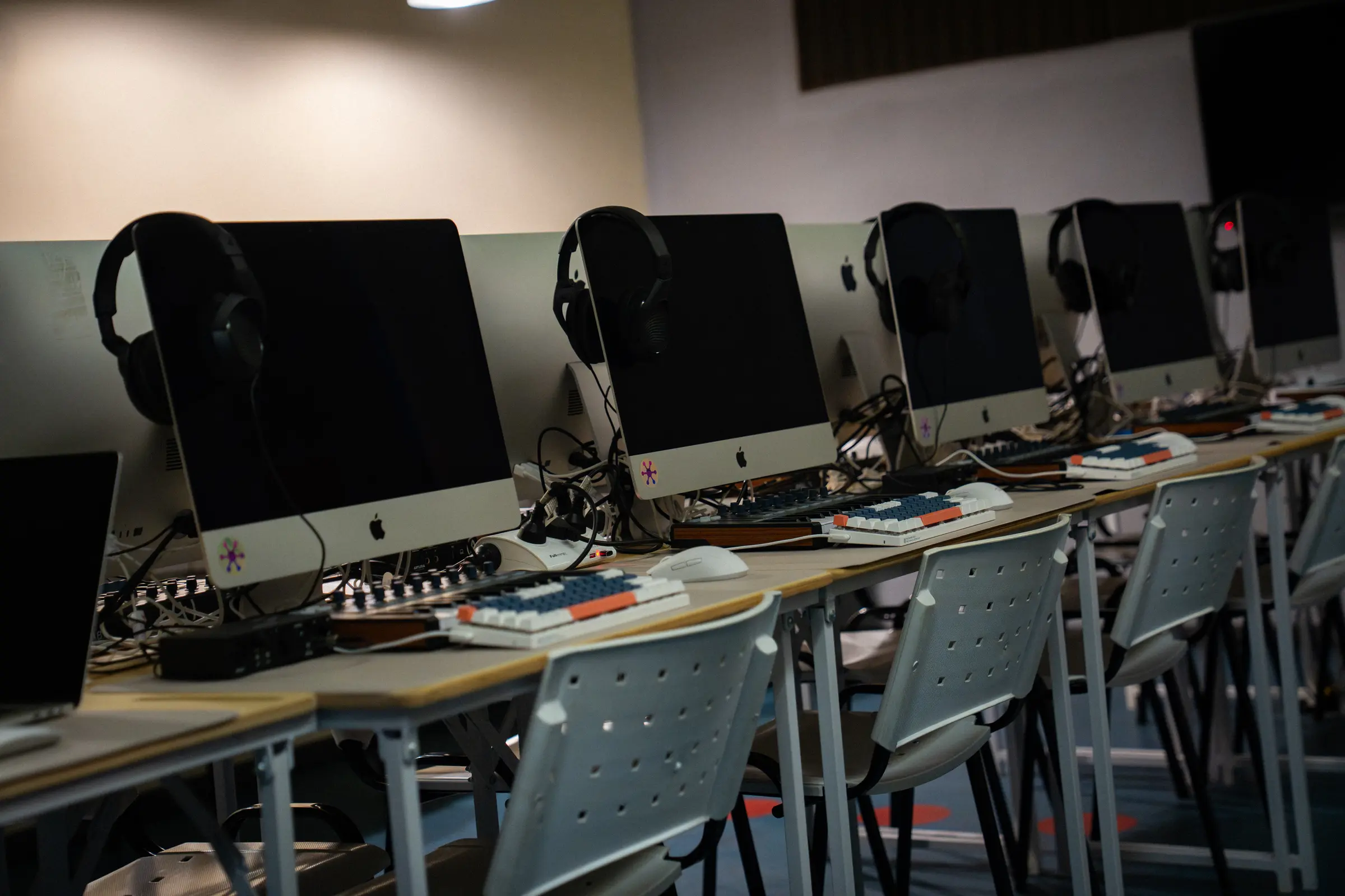 El aula de producción: filas de computadoras con auriculares y controladores