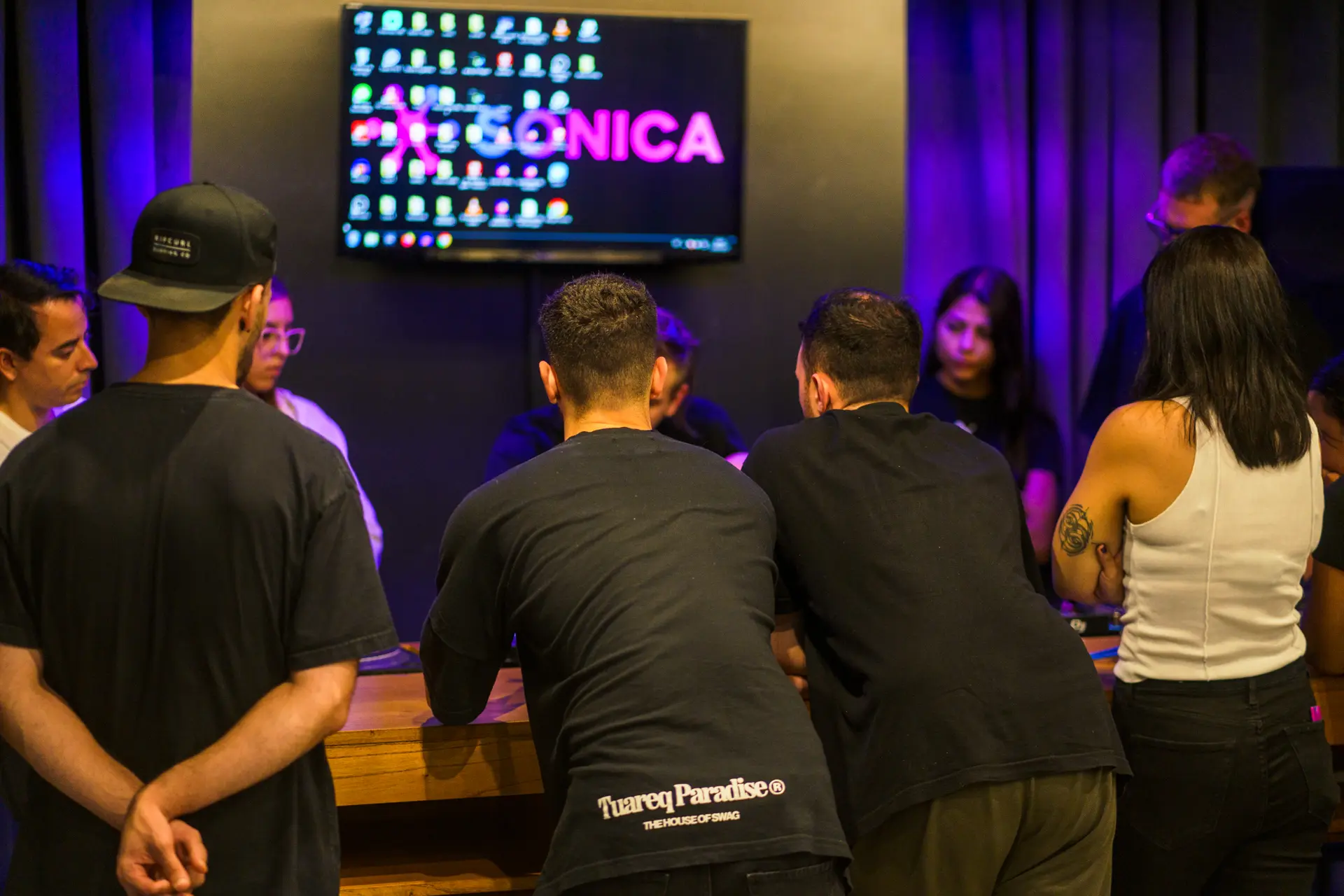 Alumnos alrededor de la cabina de DJ, frente a la pantalla con el logo de Sónica