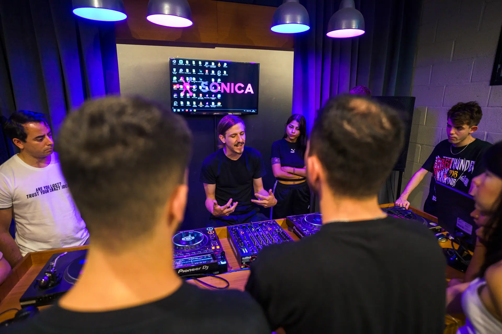 Clase de DJ: el docente explica frente a los alumnos sentados en la mesa de CDJ