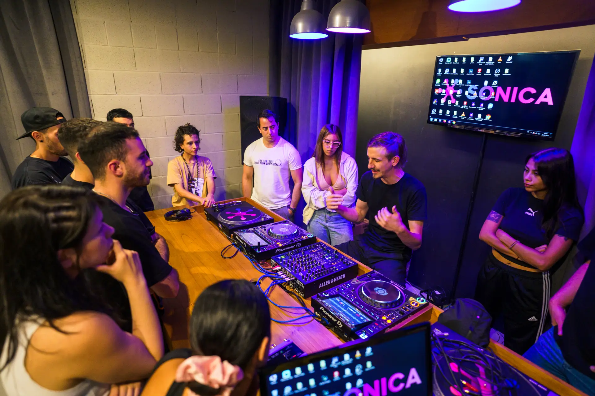 El aula de DJ completa: alumnos alrededor de la mesa de equipos bajo la luz violeta